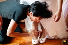 At the bride's house in Chiari (Bs), the bride is gently helped to put on her shoes by an assistant as she prepares for the wedding ceremony.